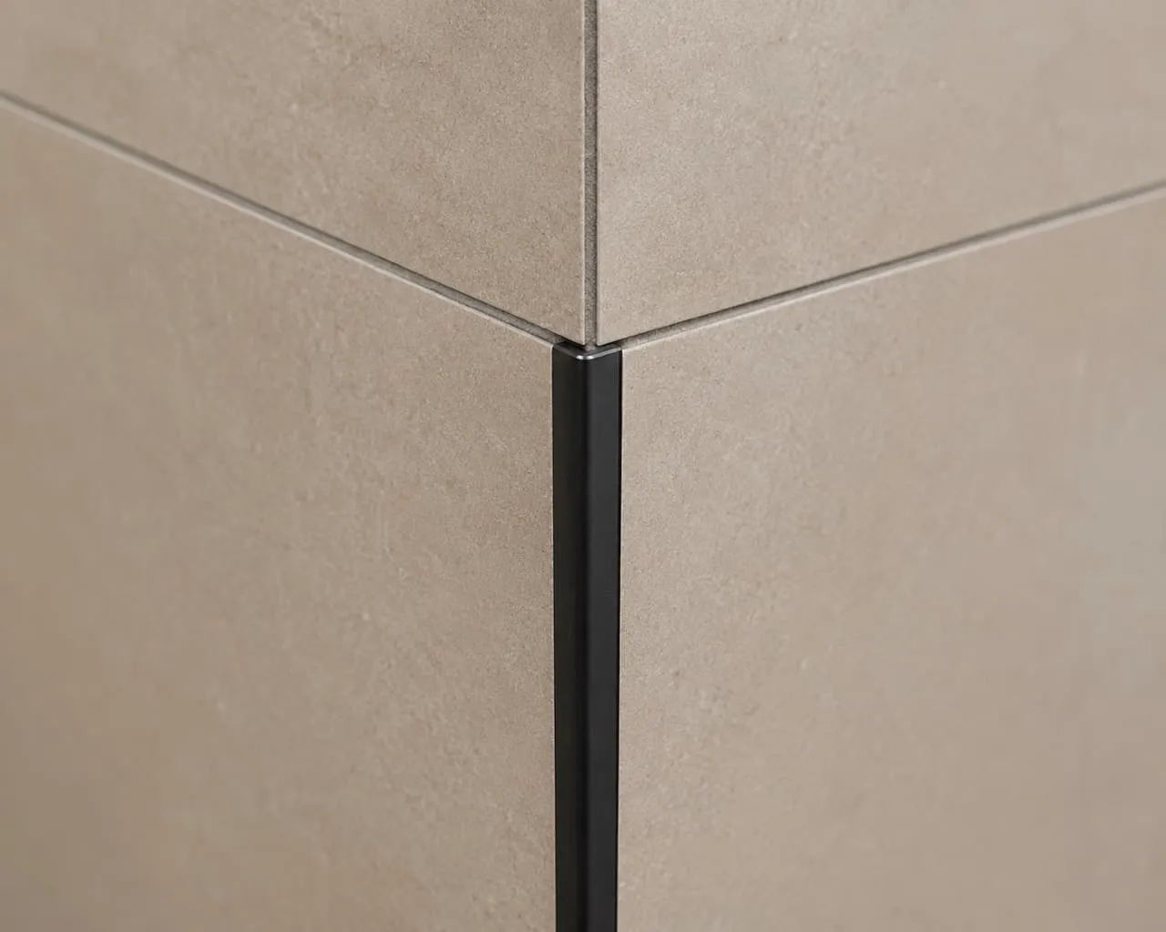 Close-up of a matte black Schluter metal edge trim finishing the raw tile transition along an outer shower wall corner