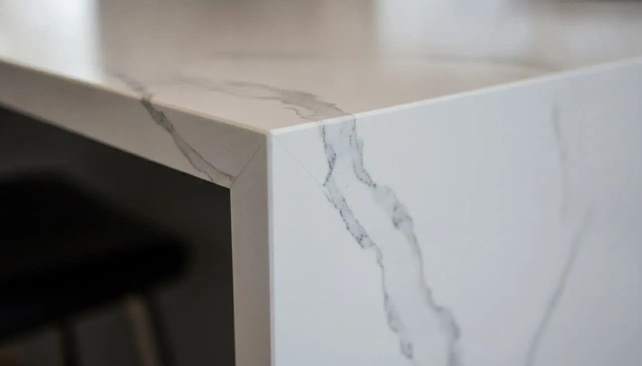 Quartz countertop waterfall corner with perfectly book-matched veining flowing continuously down the vertical side